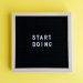 Black message board with 'Start Doing' on a bright yellow background for inspiration.